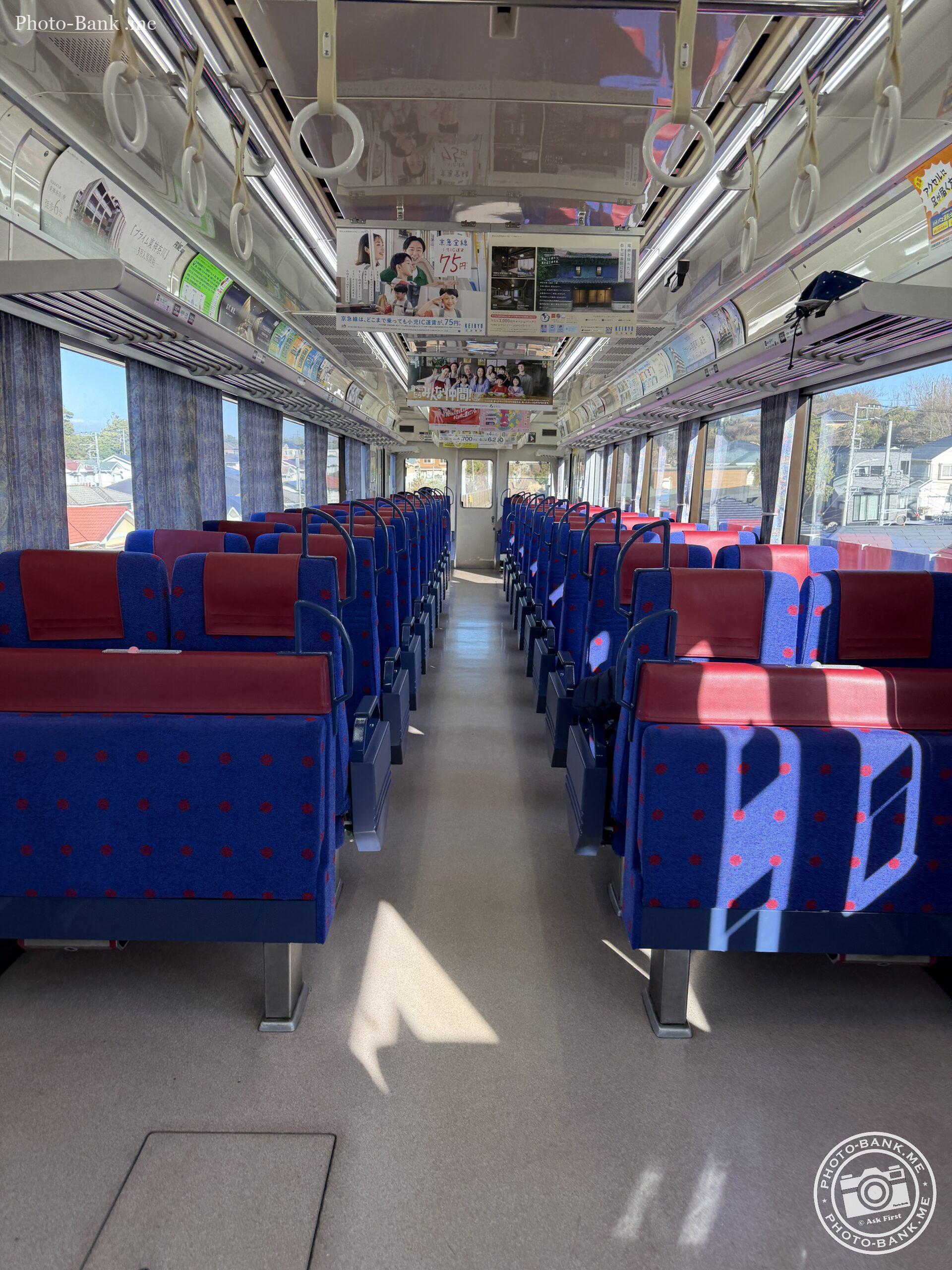 京急電鉄の車内、青と赤の座席が整然と並び、車窓からは住宅街が見える。