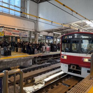 京浜急行品川駅のホームで、羽田空港行きの赤い電車を待つ乗客たち。