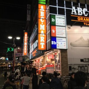 夜の横浜駅西口、ABCマートのネオンサインと行き交う人々。