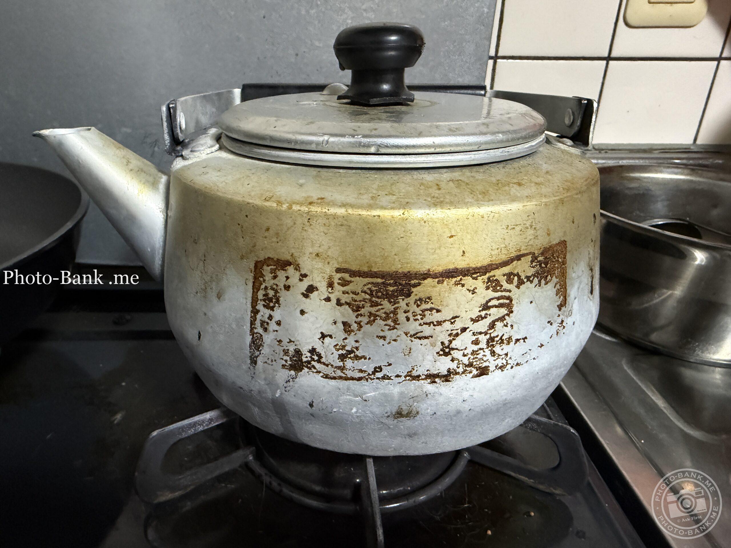 使い込まれたアルミ製やかんがガスコンロに置かれている様子。錆や焦げ付きが歴史を物語る。